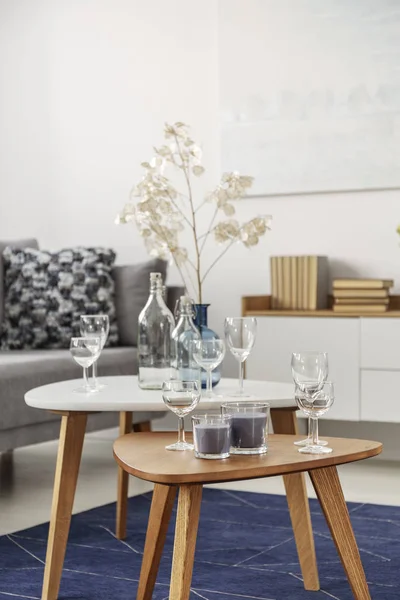 Bicchieri bianchi e candele su due tavolini da caffè in luminoso soggiorno interno — Foto Stock