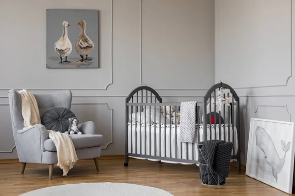 Bequemer grauer Sessel mit rundem Kissen und weißer Decke neben Holzbett mit Kissen und Spielzeug, Kopierraum an leerer Wand — Stockfoto
