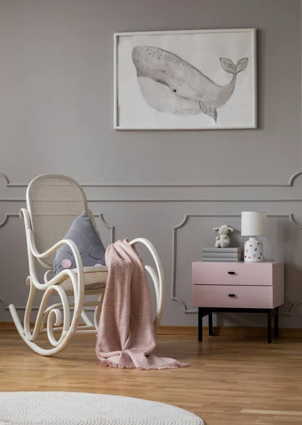 Baleia em cartaz em quarto de bebê elegante com cadeira de balanço branco e mesa de cabeceira rosa pastel com livros e lâmpada — Fotografia de Stock
