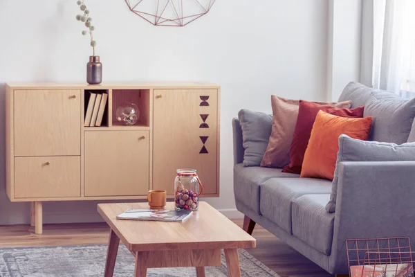 Винтажный деревянный журнальный столик и комод в элегантном интерьере гостиной с серым диваном — стоковое фото