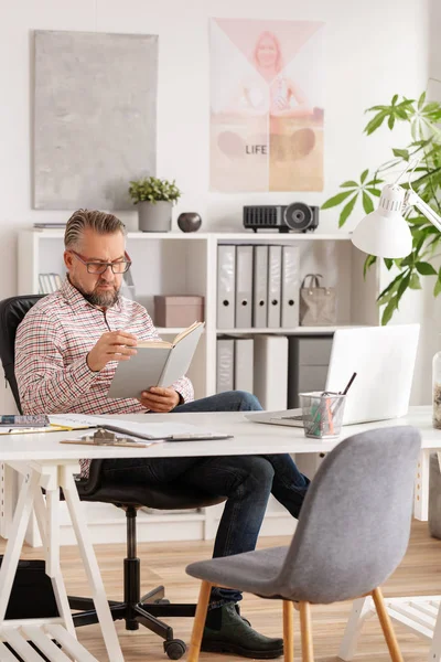 Lässig aussehende gutaussehende leitende Psychologe liest Buch in seinem Büro — Stockfoto