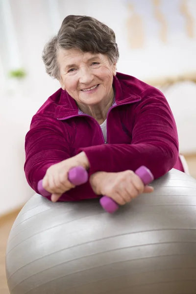 Lächelnde ältere Frau hält Gewichte in der Hand und legt sich auf den Turnball — Stockfoto