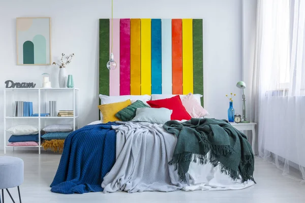 Зелені, сірі та сині ковдри на білому ліжку з райдужним ліжком в білому, скандинавському інтер'єрі спальні. Справжня фотографія — стокове фото