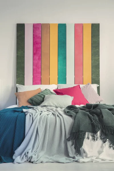 Nahaufnahme eines bunten Bettes in weißem Schlafzimmerinterieur. echtes Foto von gelben, grauen, grünen und rosa Kissen auf weißen Laken. — Stockfoto