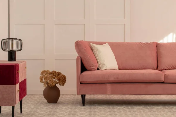 Цветы в глиняной вазе рядом с пастельно-розовым диваном с белой подушкой — стоковое фото