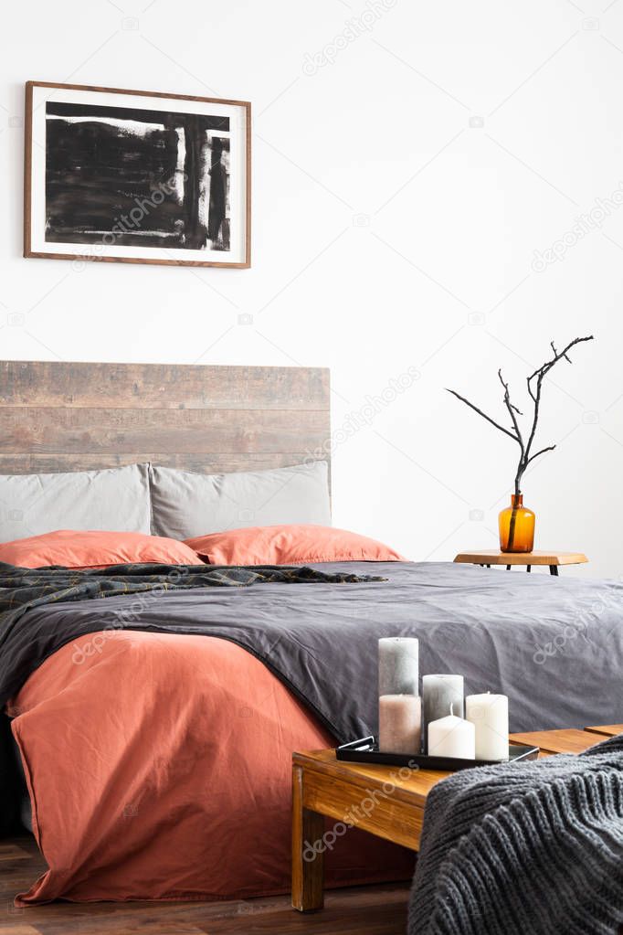 Vertical shot of wooden bed with linen bedclothes, artwork and o
