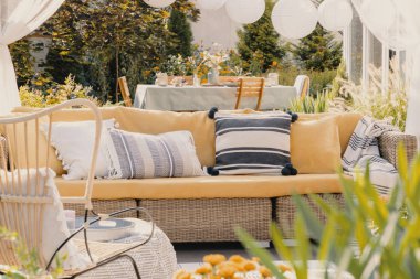 Bahçede hasır bir kanepede desenli yastıklar. Bir bitkinin bulanık yakın çekim. Gerçek fotoğraf