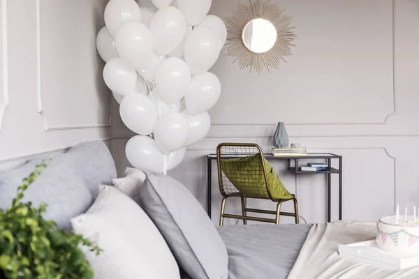Lot de ballons blancs à l'intérieur de la chambre à coucher tendance avec commode industrielle avec miroir doré et chaise avec oreiller vert et lit avec literie grise et gâteau d'anniversaire — Photo