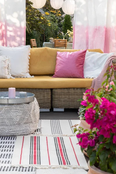 Primo piano di fiori rosa su una terrazza con un divano di vimini e cuscini sullo sfondo. Foto reale — Foto Stock