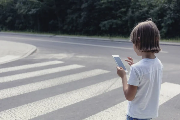 School jongen op voetgangers kruising kijken naar zijn telefoon — Stockfoto