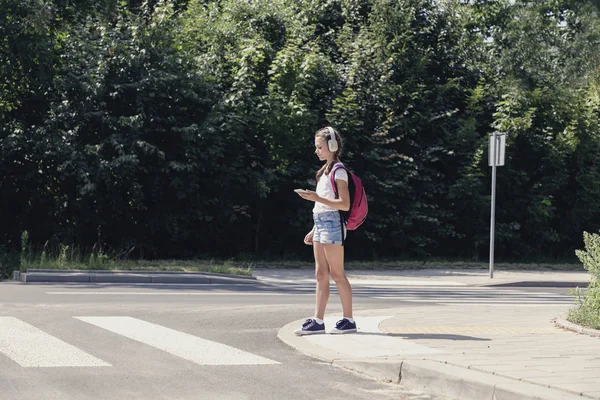 Estudante muito adolescente com fones de ouvido e telefone celular na travessia de pedestres — Fotografia de Stock