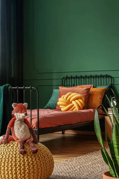 Zabawka lis siedzący na żółtym PUF w prawdziwym zdjęciu dziecięcej sypialni z zielonymi ścianami i pomarańczowymi arkuszami — Zdjęcie stockowe