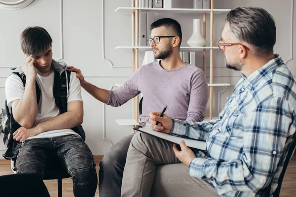 Jongeman in bril troosten zijn depressieve vriend tijdens een ontmoeting met counselor — Stockfoto