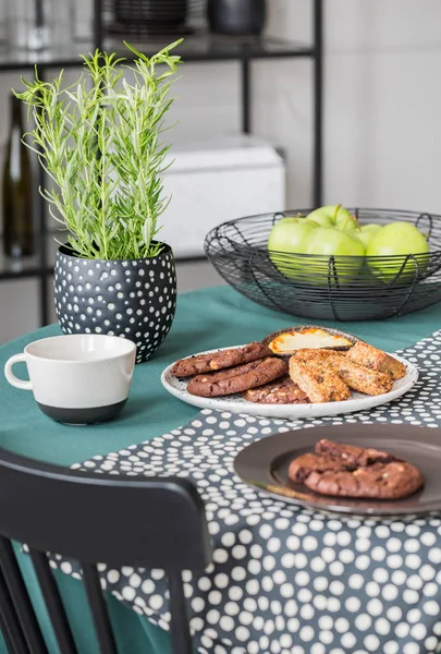 Bolinhos na placa, maçãs na tigela e planta verde na panela na mesa da sala de jantar — Fotografia de Stock