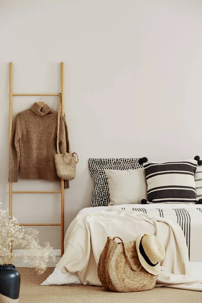 Escalera de madera con suéter y bolsa junto a la cama king size con ropa de cama a rayas — Foto de Stock