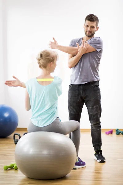 Mujer rubia de mediana edad haciendo ejercicio en la pelota de gimnasia durante la sesión con el fisioterapeuta —  Fotos de Stock