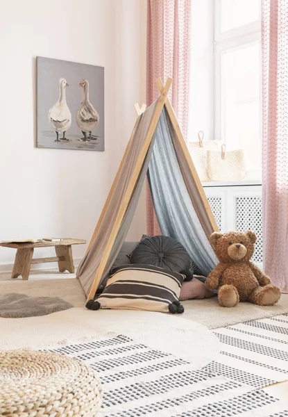 Urso de pelúcia ao lado da tenda com almofadas no interior do quarto do miúdo com cartaz, tapete e pufe. Foto real — Fotografia de Stock