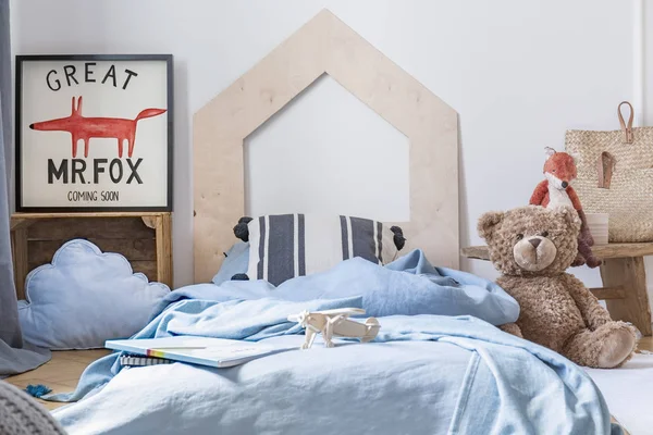 Oso de peluche junto a la cama azul con sábanas en el interior del dormitorio de los niños con cartel de zorro. Foto real — Foto de Stock