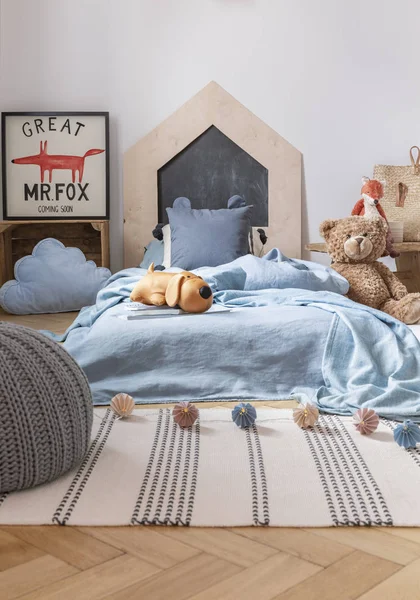 파란색 침대와 포스터 옆에 테디 베어가있는 어린이 침실 인테리어의 줄무늬 양탄자에 푸프. 실제 사진 — 스톡 사진