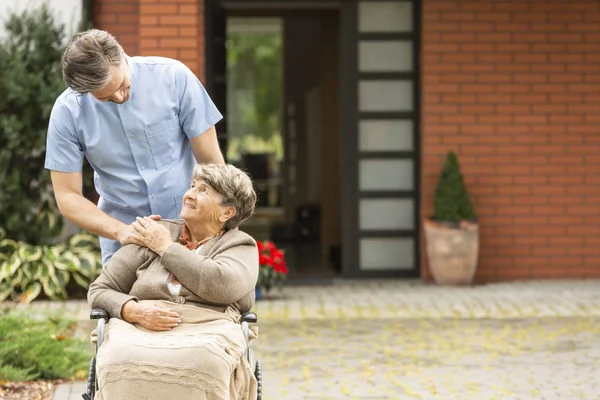 Mannelijke verpleegster helpen gelukkig oudere vrouw in de rolstoel in de voorkant van het huis — Stockfoto