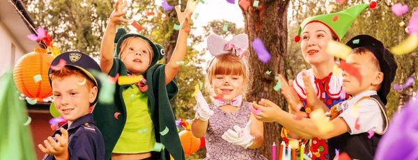 Pemandangan panorama animator dan anak-anak menikmati hujan confetti selama ulang tahun berdandan pesta di kebun — Stok Foto