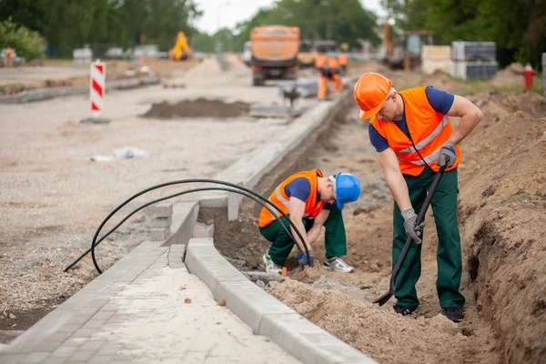 Dos trabajadores en chaqueta de seguridad naranja en una construcción de carreteras, la industria y el trabajo en equipo —  Fotos de Stock