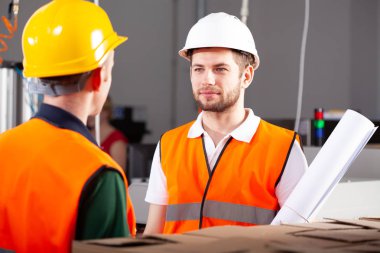 Turuncu ceketli ve beyaz kasklı yakışıklı bir fabrika işçisi.