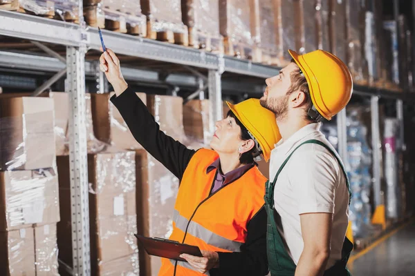 Two warehouse workers in green uniforms and yellow safety helmets — Stock Photo, Image