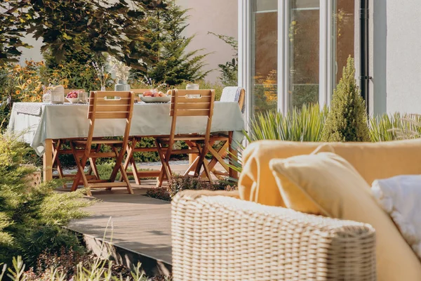 Holzstühle am Tisch auf der Terrasse des Hauses mit Pflanzen und Rattanmöbeln im Sommer. echtes Foto — Stockfoto