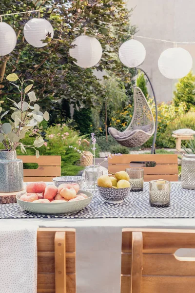 Lanterns above table with food and drink in the garden with plants and wooden chairs. Real photo — Stock Photo, Image
