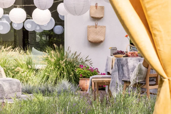 Gula gardiner och vita lyktor i trädgården med frukt på bord, blommor och väskor. Verkligt foto — Stockfoto