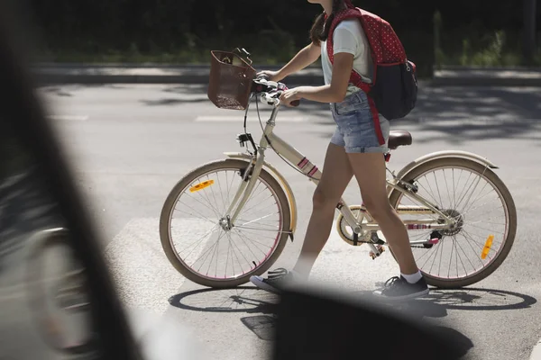 Schoolgirl with backpack and bike crossing street in front of a car — Stock Photo, Image