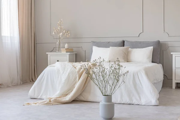 Białe kwiaty w wazonie w eleganckiej szarej sypialni wnętrze z prostym łóżku — Zdjęcie stockowe