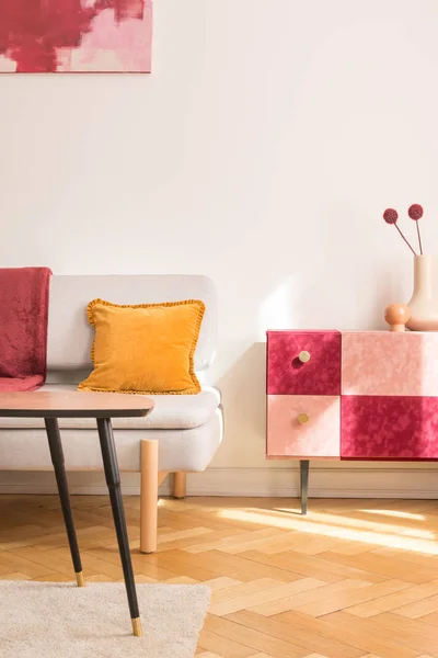 Yellow pillow on sofa next to red and pink cupboard with flowers in flat interior with table. Real photo — 스톡 사진