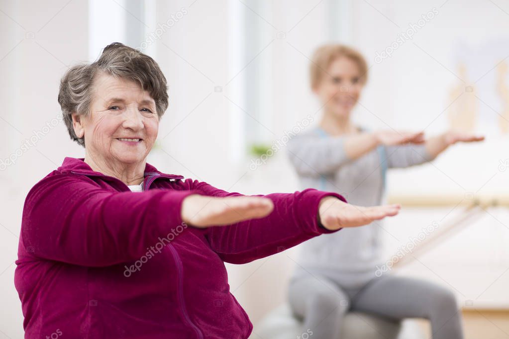 Smiling elderly lady holding her arms during pilates for seniors