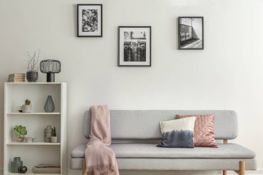 Üzerinde bitkiler ve vazolar olan beyaz ahşap bir kitaplık. Yanında gri bir kanepe ve pastel pembe battaniye.