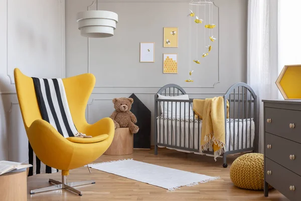 Yellow armchair, teddy bear and crib in a modern kid room interior. Real photo