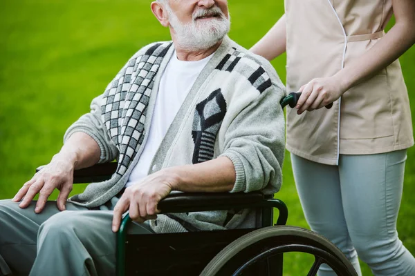 Enfermera con paciente en silla de ruedas caminando en el jardín — Foto de Stock