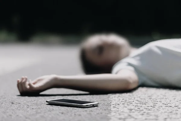 Zamazany obraz nastoletniej dziewczyny z telefonem komórkowym leżącego na ulicy po straszliwym wypadku samochodowym — Zdjęcie stockowe