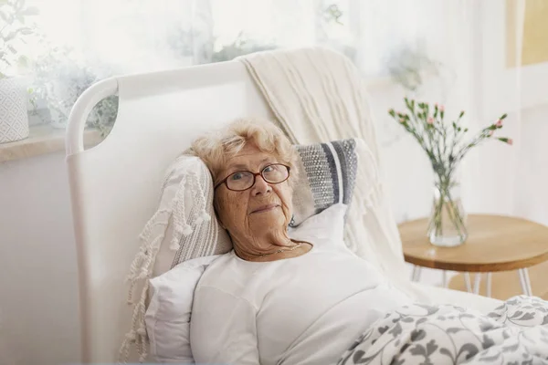 Malade femme âgée avec des lunettes couché dans le lit d'hôpital — Photo