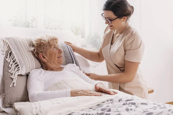 Donna anziana in ospedale letto con assistente sociale aiutarla — Foto Stock