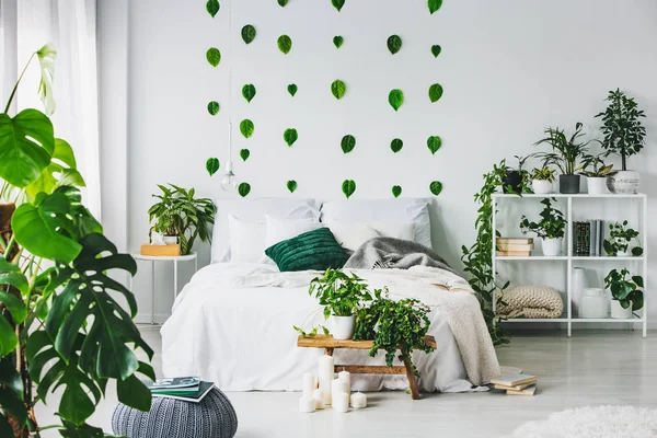 Weiße Schlafzimmereinrichtung mit King-Size-Bett mit Kissen und Decke, Stadtdschungel und grünen Blättern an der Wand — Stockfoto