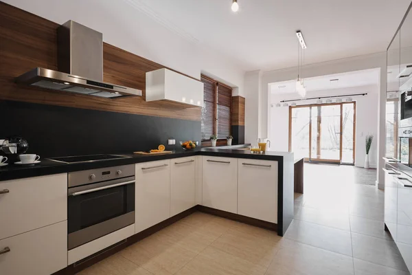 Бело-черная кухня с деревянными акцентами и открытое пространство пустой гостиной с окнами от пола до потолка — стоковое фото