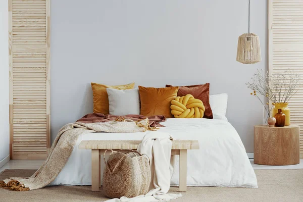 Wooden bench before king size bed with pillows and blanket, copy space on empty wall — 스톡 사진