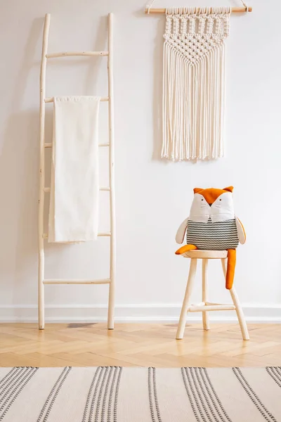 Echte foto van een ladder met een deken, speelgoed op een stoel en macrame op een muur in een natuurlijke kid kamer interieur — Stockfoto