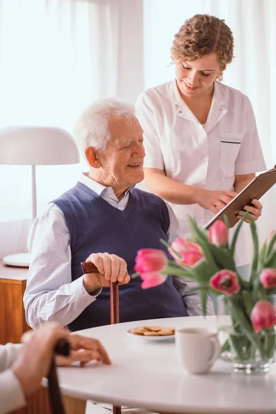 Sorrindo avô falando sobre seu horário de dia com uma enfermeira — Fotografia de Stock