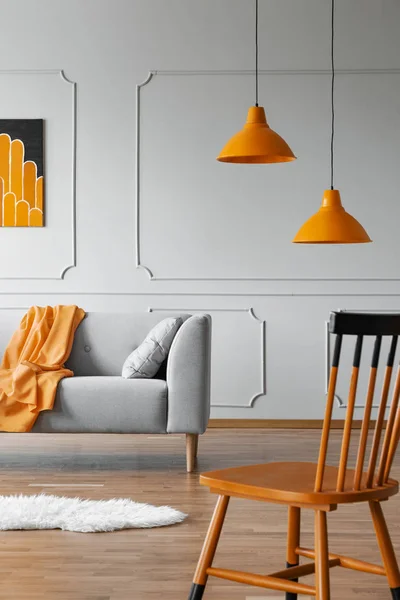 Chair in a living room interior with a wall molding, orange lamp and sofa. Real photo — Stock Photo, Image