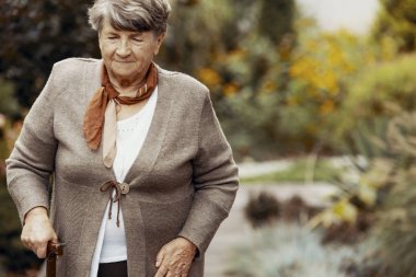 Doğanın ortasında baston ile gülümseyen yaşlı kadın