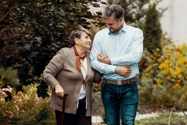 Homem de apoio mulher sênior fraco com bengala no jardim — Fotografia de Stock