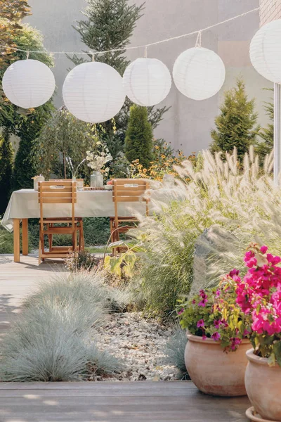 Blumen und Pflanzen auf dem Holzboden der eleganten Terrasse mit Gartenmöbeln und weißen Papierlampen, echtes Foto — Stockfoto